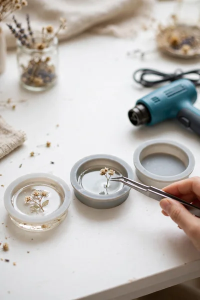 Tweezers placing a tiny dried flower into a resin filled silicone mold