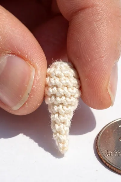 Tiny crocheted turtle tail beside a coin