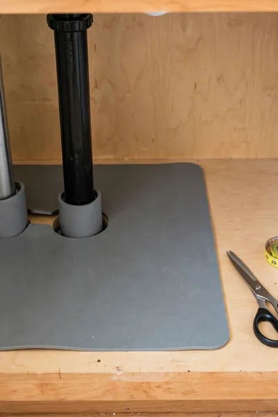 Waterproof mat being trimmed to fit an under sink cabinet floor